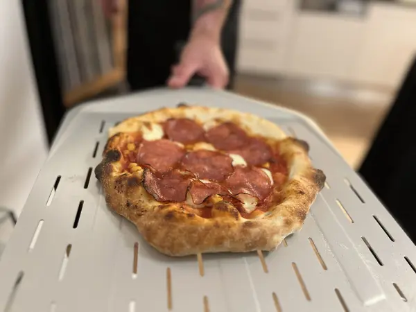 Eine frisch gebackene Pizza mit Salami wird auf einer hellen Pizza-Schaufel in einer modernen Küche serviert.