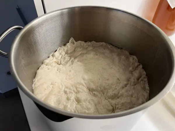 Ein großer Topf mit unerheblichem Pizzateig, der stark aufgeht, steht auf einer Küchenarbeitsplatte.