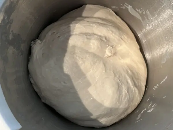 Ein Weizenteig liegt in einer Edelstahlschüssel und wartet darauf, zu einer köstlichen Pizza verarbeitet zu werden.