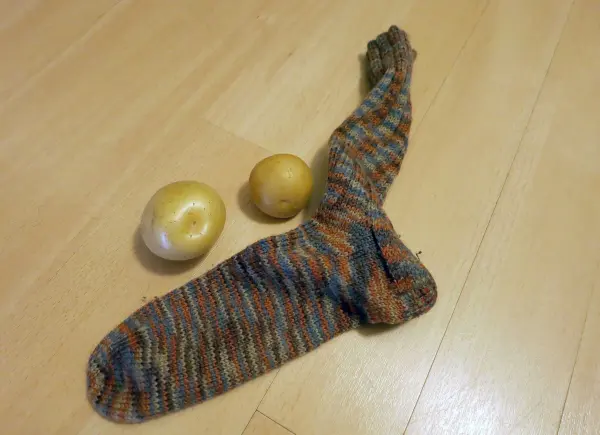 Ein gestreifter Strumpf liegt auf Holzboden, daneben zwei rohe Kartoffeln.