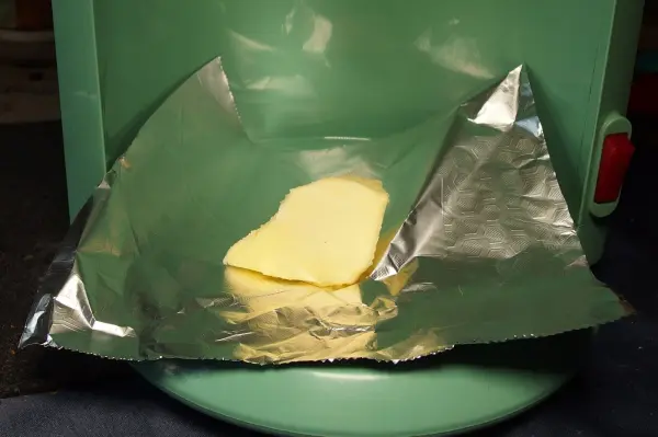 Ein Stück Butter liegt auf der Aluminiumfolie, die auf einer grünen Kaffeemaschine platziert ist, um sie zu erwärmen.