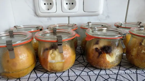 Gläser mit Bratäpfeln stehen auf einem Tisch, dampfend und bereit zum Servieren, umgeben von einer modernen Kücheneinrichtung.