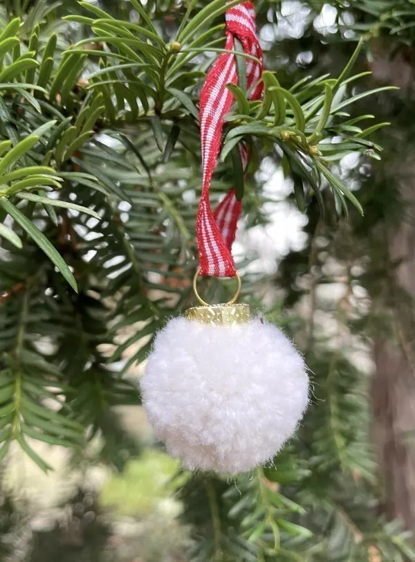 Weiße Weihnachtskugel aus selbstgemachtem Pompom an einem Tannenzweig.