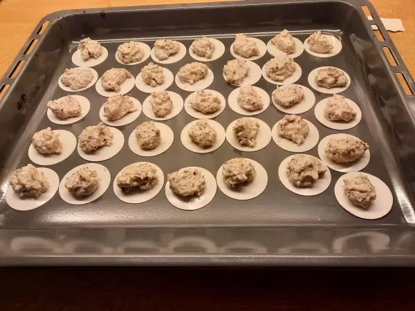 Auf einem Backblech liegen mehrere Kekshaufen aus Haselnuss und Haferflocken, bereit zum Backen in einer Haushaltküche.