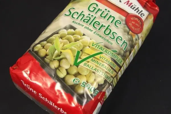 Grüne Erbsen in einer roten Verpackung liegen auf einem schwarzen Hintergrund, gekennzeichnet als gesund und ohne Salz.