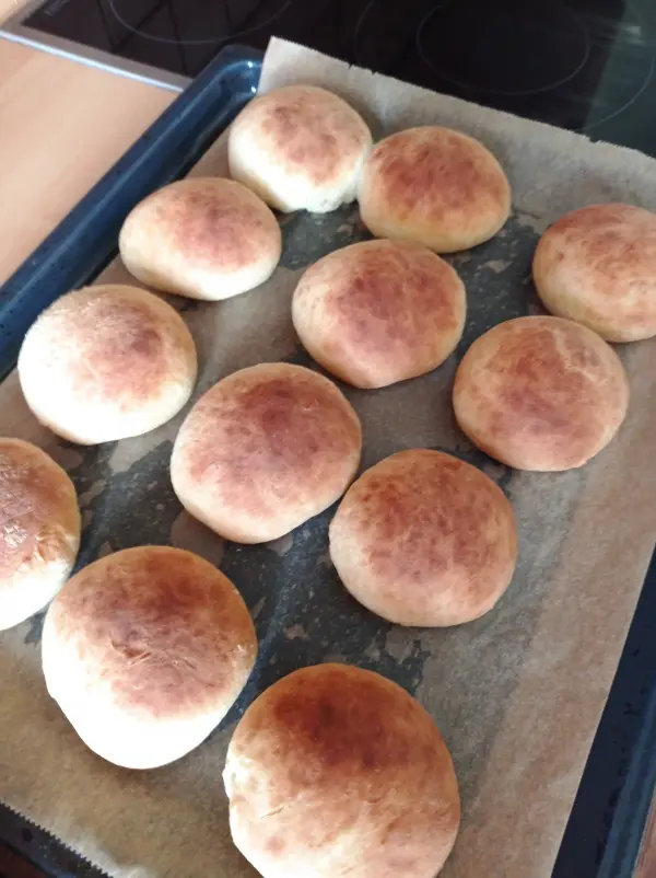 Die frisch gebackenen Brötchen liegen auf einem Blech, umgeben von Backpapier, und warten darauf, serviert zu werden.