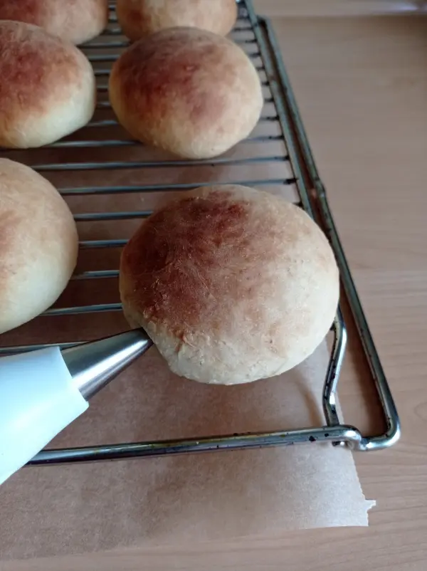 Auf einem Kuchengitter liegen frisch gebackene Berliner, während eine Spritztülle sie sanft berührt.