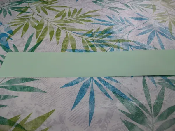Eine grüne Papierzuschnit liegt auf einem blumigen Tisch; bereit zum Basteln von Osterhasen aus Papier.