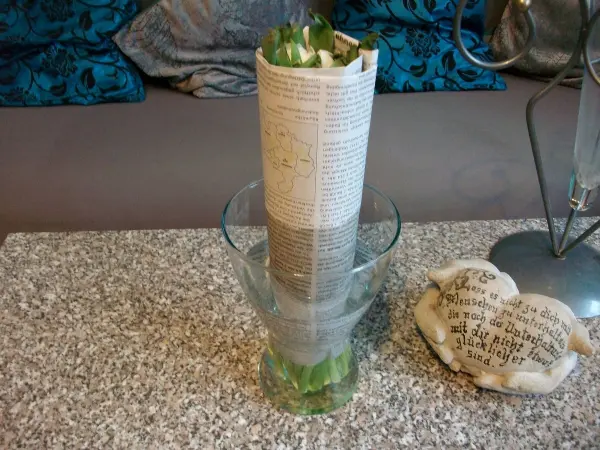Eine Vase mit frischen Tulpen, die in Zeitungspapier gewickelt sind, steht auf einem Tisch neben einem dekorativen Stein.