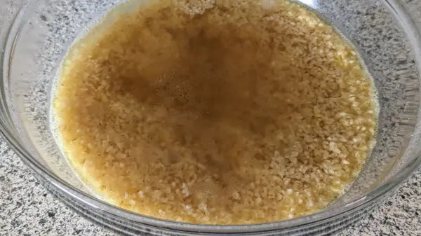 Bulgur liegt in einer Schüssel mit Wasser, um zu quellen. Die Umgebung ist eine helle, schlichte Küchenarbeitsplatte.