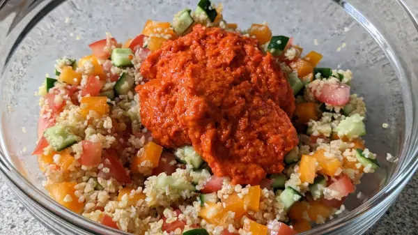 Bulgursalat mit Ajvar in einer Schüssel, kombiniert mit frischem Gemüse wie Tomaten und Gurken.
