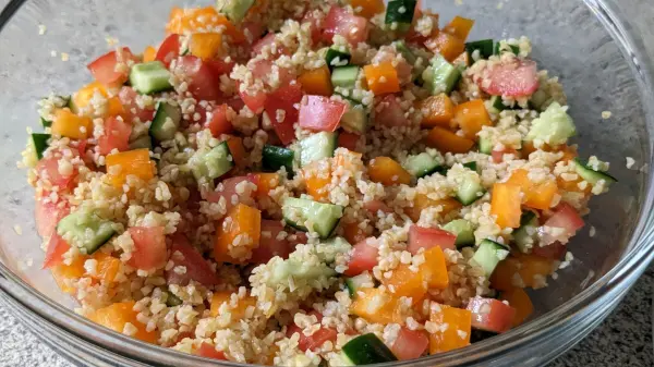 Ein bunter Bulgursalat mit Tomaten, Paprika und Gurken wird in einer Schüssel serviert, ideal für eine frische Beilage.