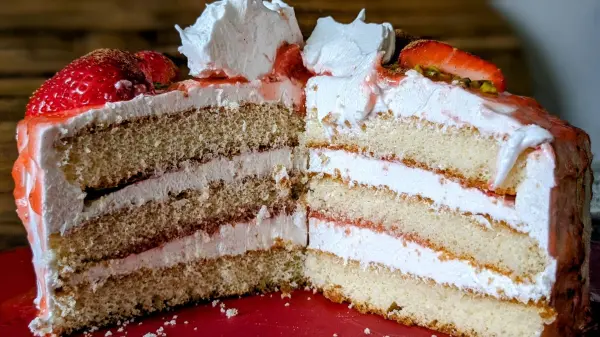 Eine kleine Geburtstagstorte mit Erdbeeren hat mehrere saftige Schichten und ist mit Sahne und Erdbeeren dekoriert.