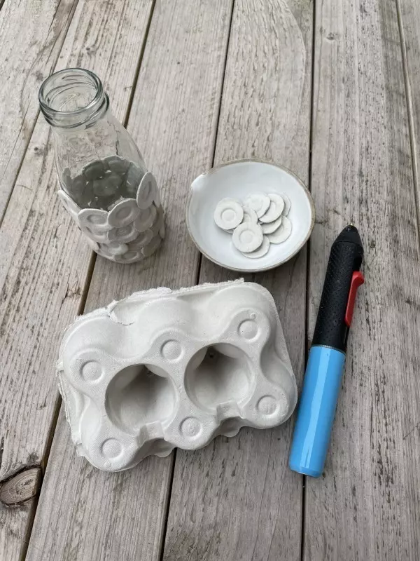 Bastelmaterialien für die Strukturvase: Eierkarton, Glasflasche und Heißklebepistole - alles, was du für das DIY-Projekt benötigst.
