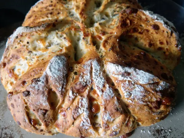 Ein frisch gebackenes Dinkelbrot mit Parmesan liegt auf einem Hintergrund, leicht mehlbestäubt und knusprig.