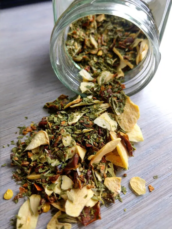 Ein Glas mit getrockneten Kräutern kippt, während der Inhalt auf eine Holzoberfläche streut, wunderbar für ein Kräuter-Pesto.