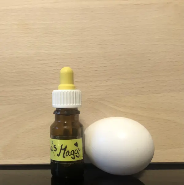 Eine kleine Flasche mit gelbem Deckel steht neben einem weißen Ei auf einem Tisch aus hellem Holz, bereit zum Mitnehmen.