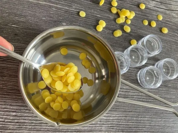 In einer Schüssel aus Edelstahl werden gelbe Bienenwachsperlen mit einem Löffel vorbereitet, um Lippenbalsam mit Honig herzustellen.