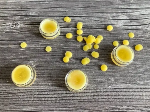 Kleine Gläser mit Lippenbalsam und gelben Wachskugeln sind auf einem rustikalen Holzuntergrund verteilt.
