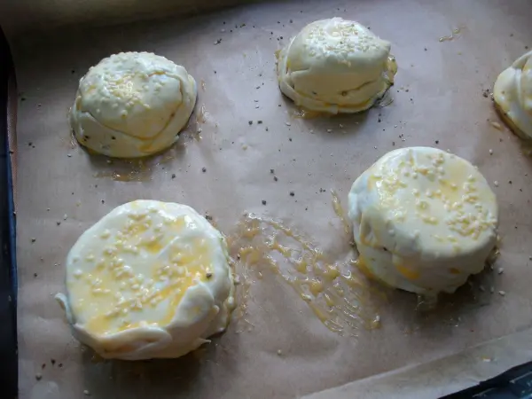 Gebackene Apfelringe aus Blätterteig mit geschmolzenem Mozzarella liegen auf Backpapier und warten auf das Backen.