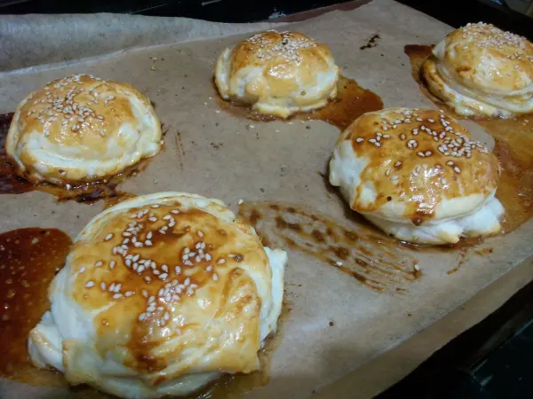 Gebackene Apfelringe aus Blätterteig und Mozzarella auf einem Backblech, goldbraun und leicht glänzend mit Sesam.