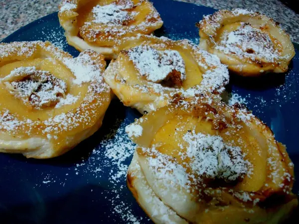 Gebackene Apfelringe sind auf einem blauen Teller angeordnet, bestäubt mit Puderzucker und goldbraun gebacken.