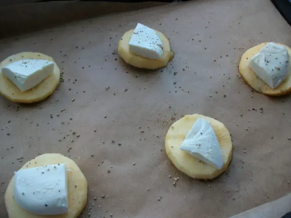 Runde Blätterteigscheiben liegen auf einem Backblech, belegt mit Mozzarella und gewürzt für gebackene Apfelringe.