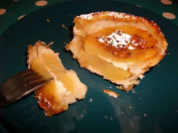 Gebackene Apfelringe mit Blätterteig und Mozzarella auf einem Teller, halb geschnitten, mit glänzender Füllung.