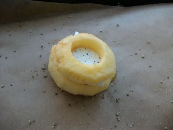 Gebackene Apfelringe liegen auf einem Backblech, gefüllt mit Mozzarella und umgeben von Bröseln.