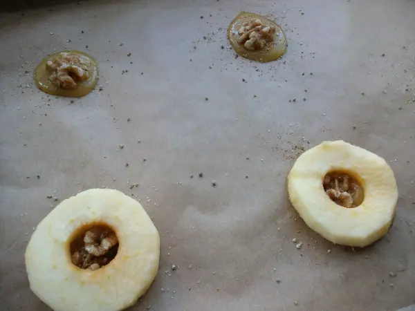 Gebackene Apfelringe liegen auf Backpapier, gefüllt mit Nüssen und Zimt, bereit zum Backen im Ofen.
