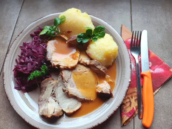 Zart geschnittenes Salzbraten mit Honig-Senf-Kruste auf einem Teller, umgeben von Rotkraut und knusprigen Knödeln.