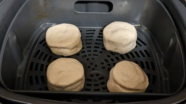 Vier rohrförmige Teigstücke liegen in einer Heißluftfritteuse und warten darauf, gekocht zu werden.