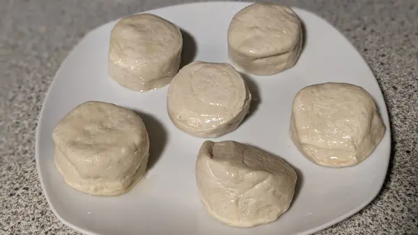 Sechs ungebackene Teigstücke auf einem weißen Teller, bereit zum Frittieren in einer Heißluftfritteuse.