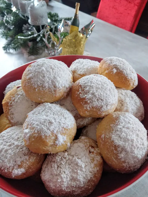 In einer großen roten Schüssel liegen frisch zubereitete Berliner mit Puderzucker auf der Oberfläche, umgeben von festlicher Deko.