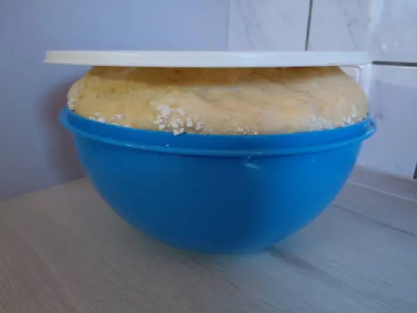 Der große Teig in einer blauen Schüssel wächst unter einem weißen Deckel auf einem hellen Tisch, bereit für Berliner aus der Heißluftfritteuse.