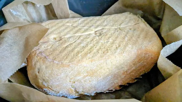 Ein lauwarmer Laib Dinkel-Weizen-Roggenbrot ruht in braunem Papier in einer Heißluftfritteuse und wartet auf den Verzehr.