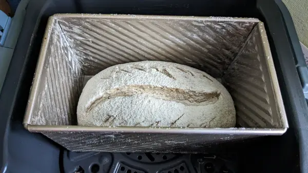 Ein Laib Dinkel-Weizen-Roggenbrot ruht in einer Backform in der Heißluftfritteuse, bereit zum Backen.