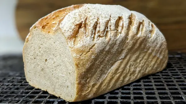 Ein frisch gebackenes Dinkel-Weizen-Roggenbrot ruht auf einem Gitter und zeigt eine goldene, knusprige Kruste.