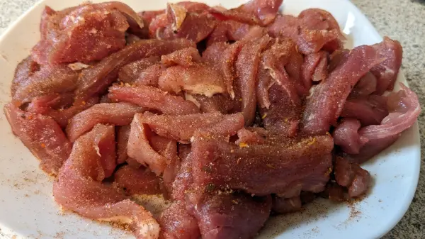 Mariniertes Schweinefilet wird auf einem Teller präsentiert, bereit für die Zubereitung in einer Gemüsepfanne.