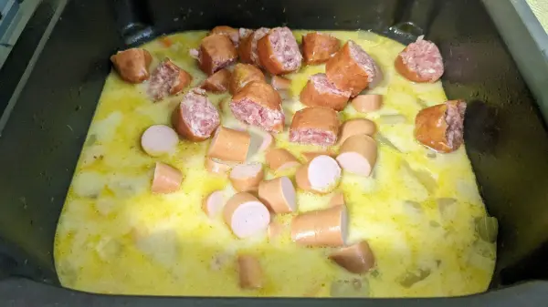 Ein Gemüseeintopf wird in einer Heißluftfritteuse zubereitet, mit Wurststücken in brüheartiger Flüssigkeit.