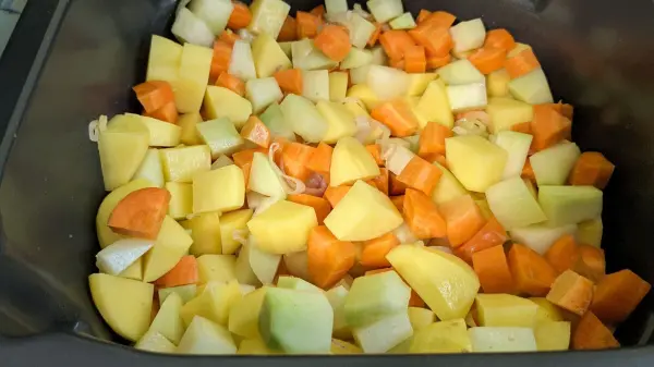 Bunte Stücke aus Kartoffeln, Karotten und Zucchini liegen in der Heißluftfritteuse und warten darauf, zu einem Gemüseeintopf zu werden.