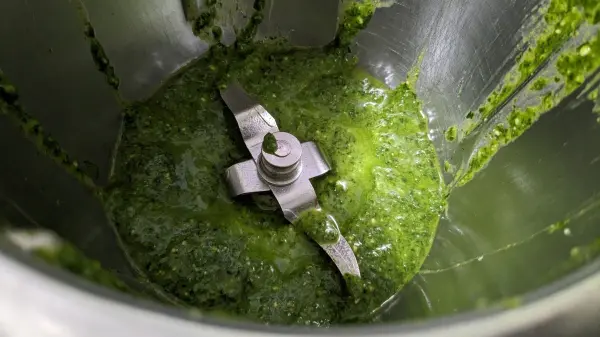Grünes Bärlauchpesto wird in einer Küchenmaschine zubereitet, während die Klingen das frische Gemüse zerkleinern.