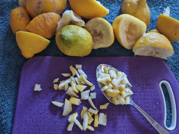 Auf einem violetten Schneidebrett liegen klein gehackte Zitronenstücke, umgeben von verschiedenen ganzen Zitronen.