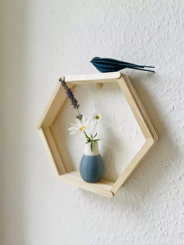 Selbstgebasteltes Holz-Sechseckregal hält eine kleine Vase mit Blumen und ein dunkelblauer Vogel aus Papier sitzt obenauf.