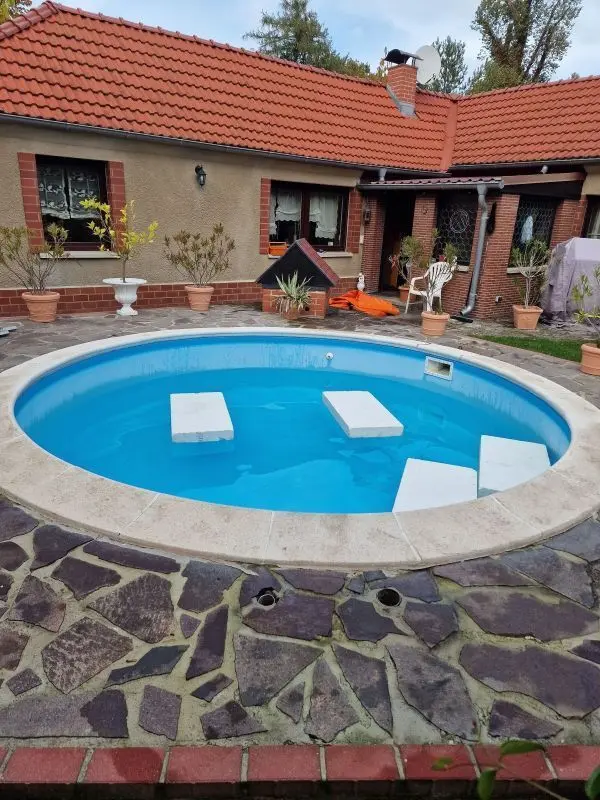 Ein runder Pool mit klarem Wasser steht in einem Garten, umgeben von einem gepflegten Gelände und einem gemütlichen Haus.