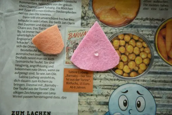 Zwei Filzstücke liegen auf einer Zeitung. In der Mitte ist ein Tropfen Heißkleber.