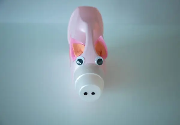 Eine Plastik-Waschmittelflasche, gestaltet als rosa Schwein mit Wackelaugen und Filzohren, liegt auf einem weißen Hintergrund.