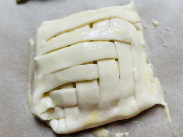 Die geflochtene Apfeltaschen aus Blätterteig wird vor dem Backen mit Eigelb bestrichen.