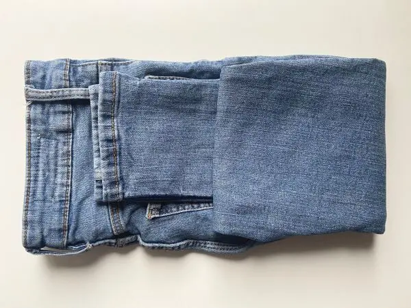 Falte deine Jeans einmal zur Mitte hoch und im Anschluss ein zweites Mal, um ein kleines Päckchen zu erhalten.