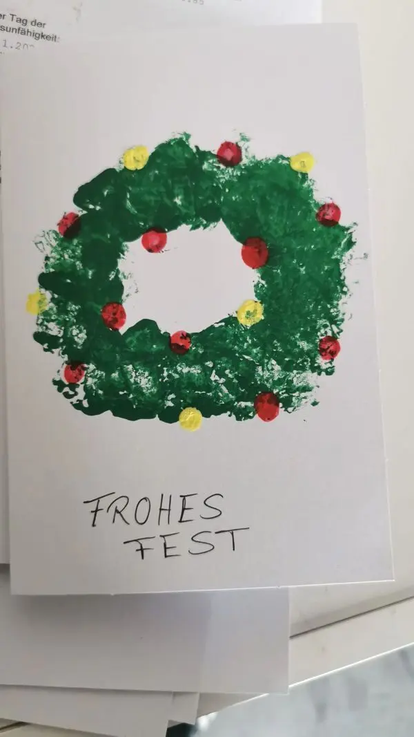 Gestalte individuelle Weihnachtskarten mit einem persönlichen Touch. Der selbstgemachte Kranz auf der Karte symbolisiert Freude und Gemeinschaft in der festlichen Zeit.